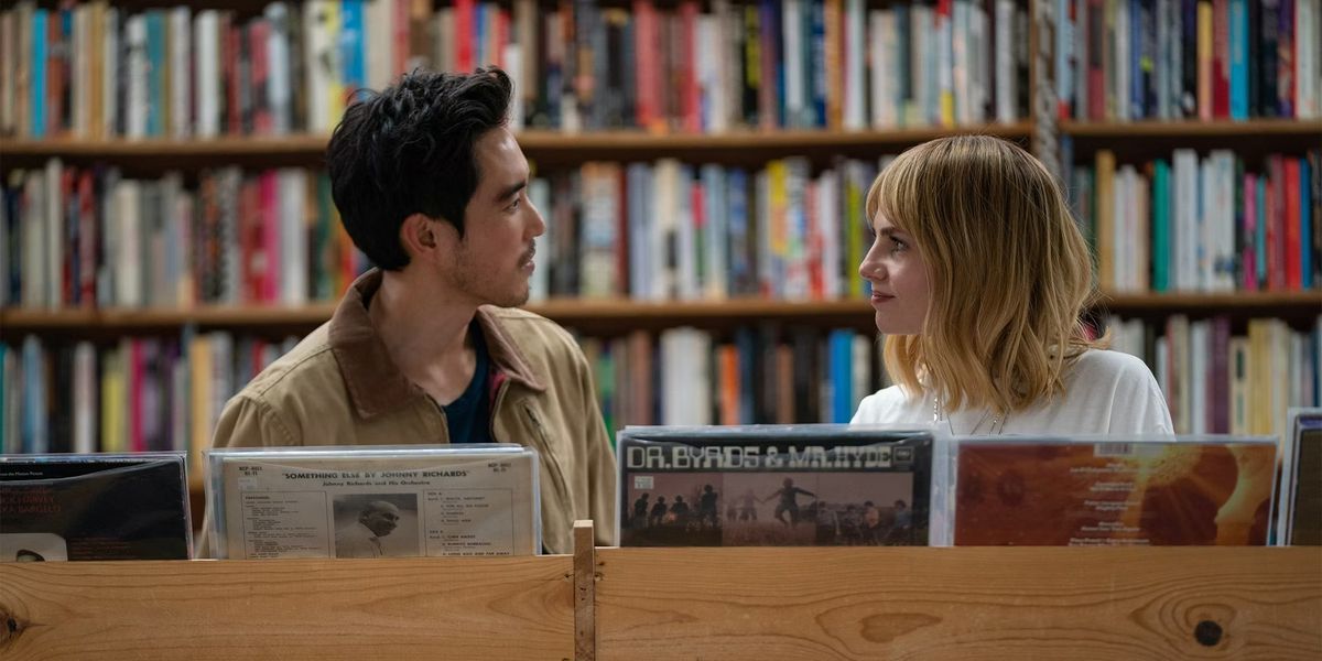 A man staring across at a woman in front of a shelf of vinyl records.